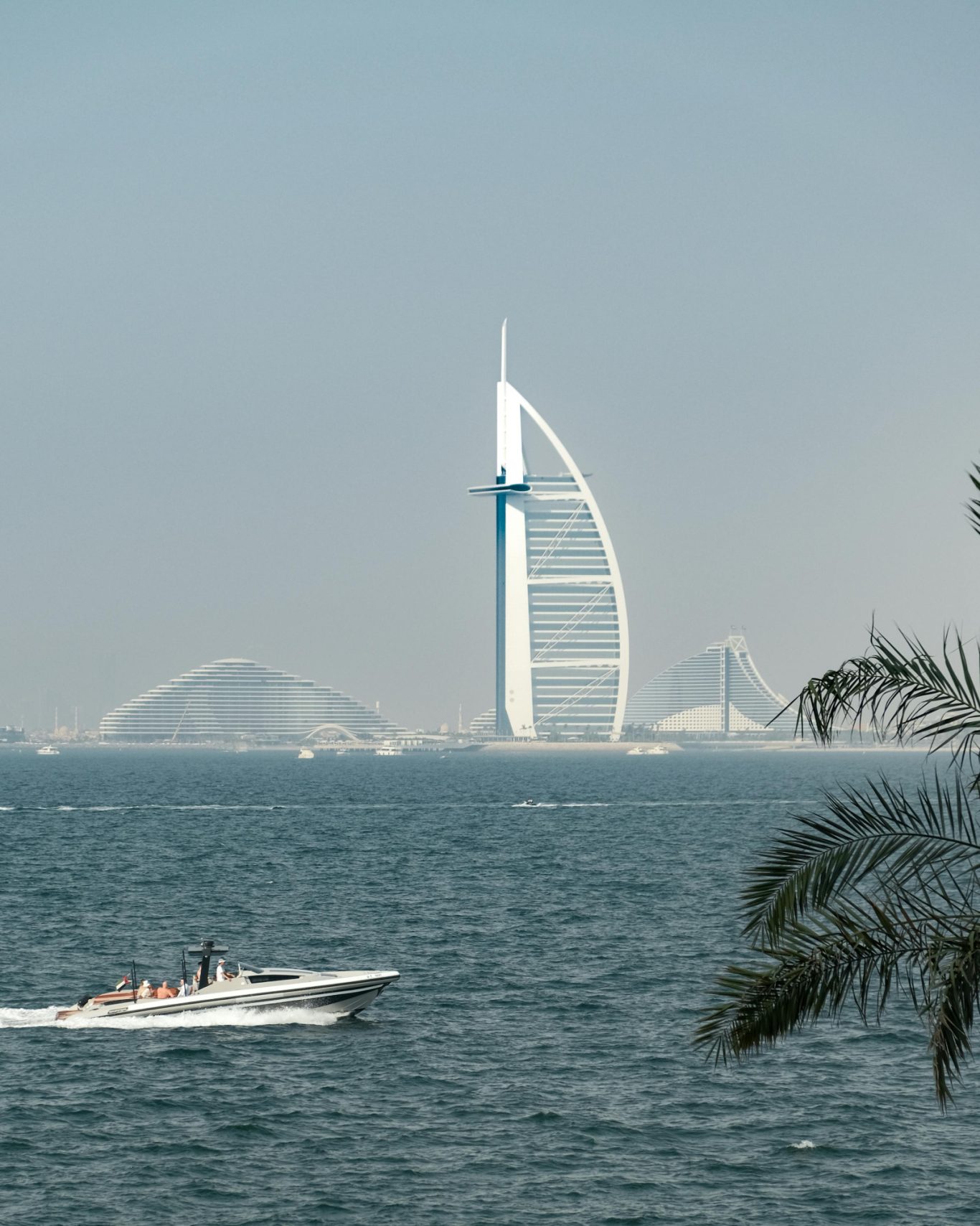 Vue sur le Burj Al Arab et un bateau sur la mer, avec des palmiers au premier plan.