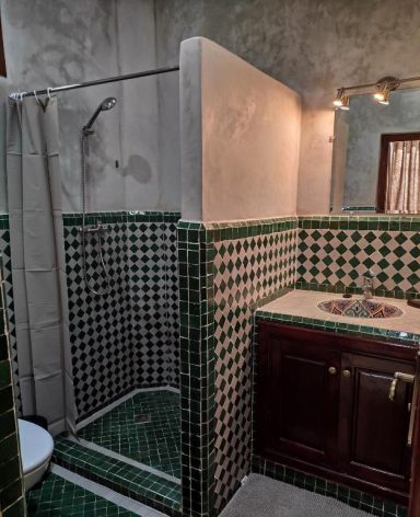 Salle de bain avec douche carrelée, lavabo en bois et murs texturés.