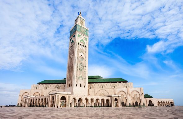 Grande mosquée avec un minaret élevé et un ciel bleu parsemé de nuages.